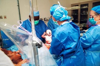 OB doctor holding newborn on operating table