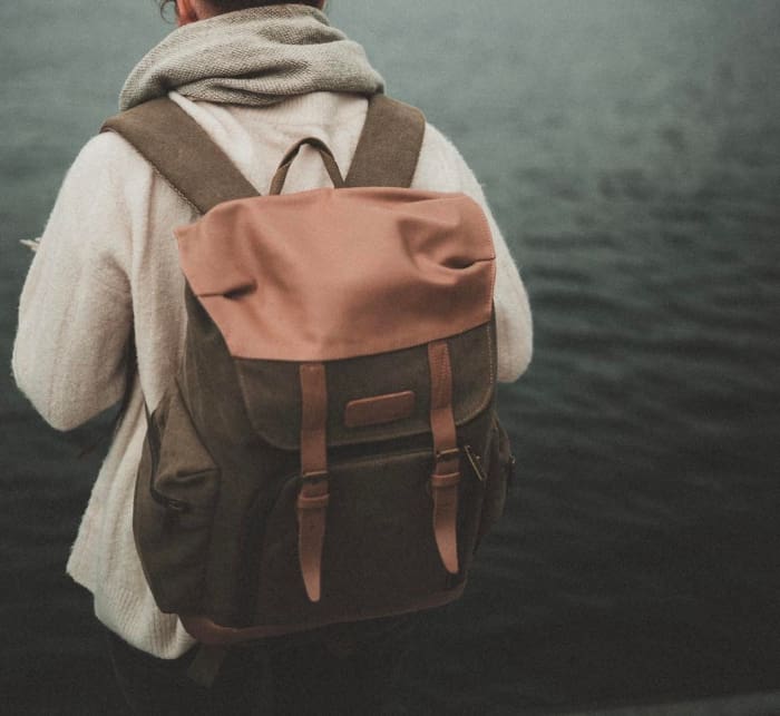 Woman standing in front of a lake with a backpack.