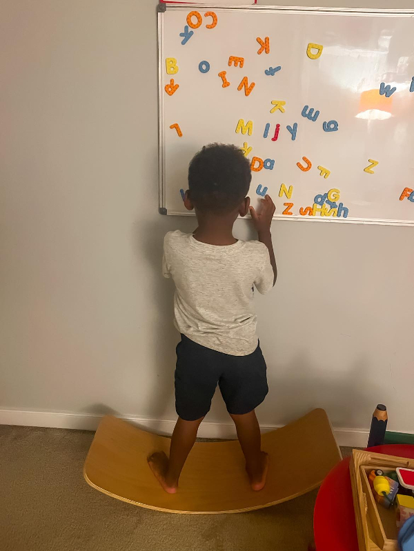 Toddler standing on balance board working with letters.