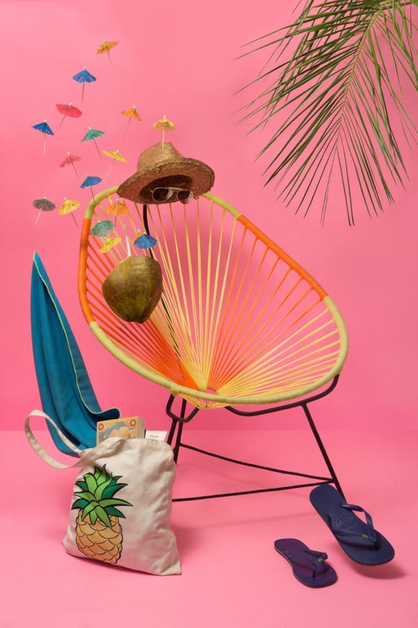 Pink background with wicker chair, straw hat and beach bag.